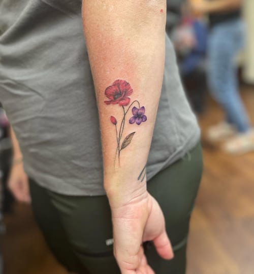 A delicate fine line flower bouquet tattoo on the forearm, featuring colorful red and purple flowers — by Sandra Price, los angeles
