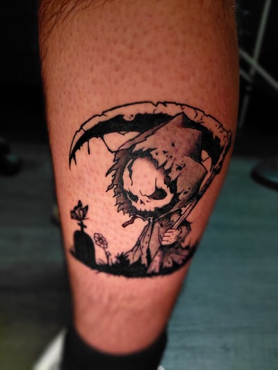 A black and grey illustrative tattoo of a cartoonish grim reaper with a scythe on the calf, featuring bold outlines and dark shading — by anoetic.designs.ultd, los angeles