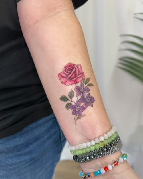 A delicate color tattoo of a rose and violet flowers on the forearm, featuring fine line and botanical style — by Melanie Benoit, los angeles