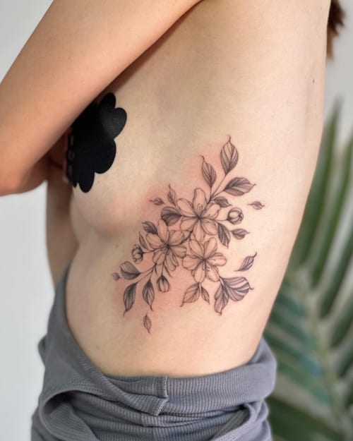A delicate black and grey floral bouquet tattoo on the rib, featuring fine line work and soft shading — by Melanie Benoit, los angeles