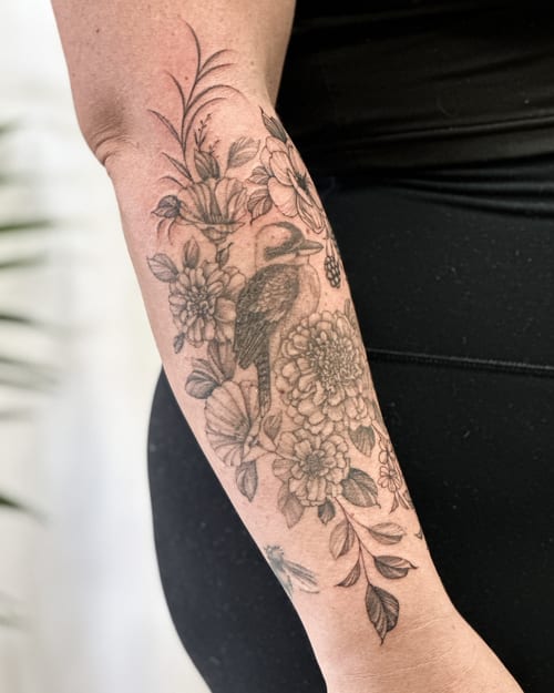 A delicate black and grey tattoo of a bird surrounded by flowers on the forearm, featuring fine line details and ornate floral elements — by Melanie Benoit, los angeles