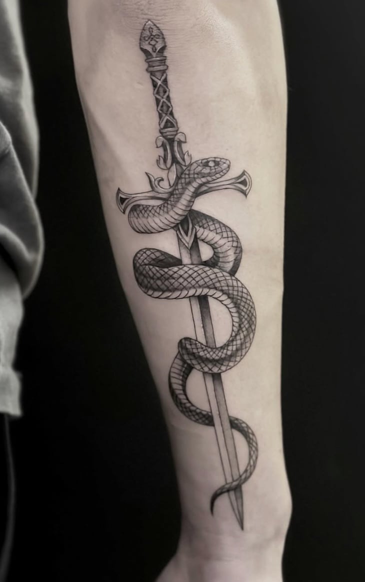 A black and grey tattoo of a realistic snake coiled around a sword on the forearm, featuring detailed shading and linework — by Jian Liang, los angeles
