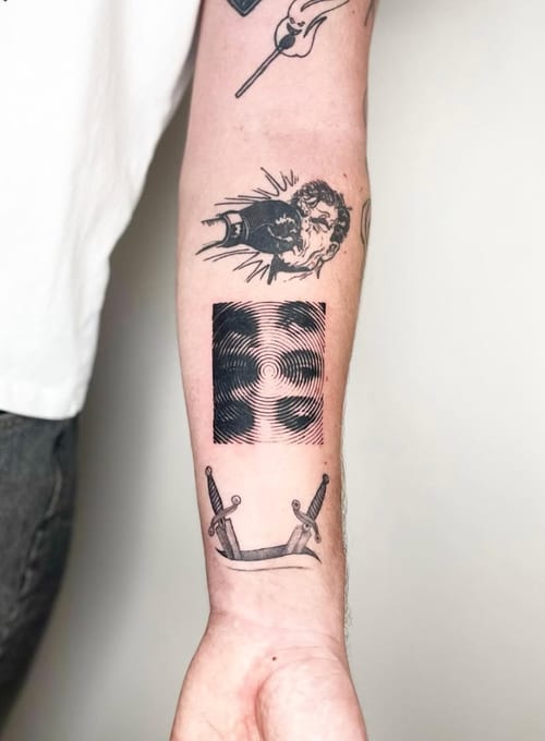 A black and grey abstract tattoo on the forearm featuring a geometric pattern, a stylized face, and two swords — by Level tattoo, los angeles