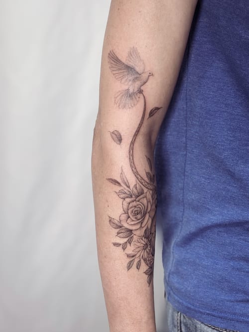 A delicate black and grey tattoo of a dove and floral arrangement on the forearm, featuring fine line work and roses — by Melanie Benoit, los angeles