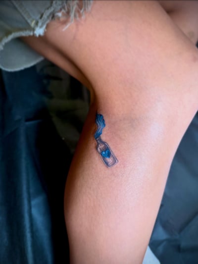 A small minimalist tattoo of a bottle with a heart inside on the ankle, using fine line and color — by zitronxus, los angeles