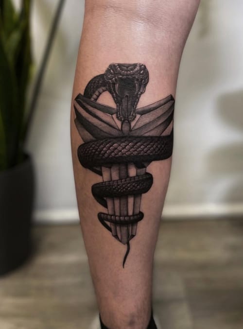 A black and grey tattoo of a snake wrapped around a dagger on the calf, featuring detailed dotwork and bold black lines — by Jian Liang, los angeles