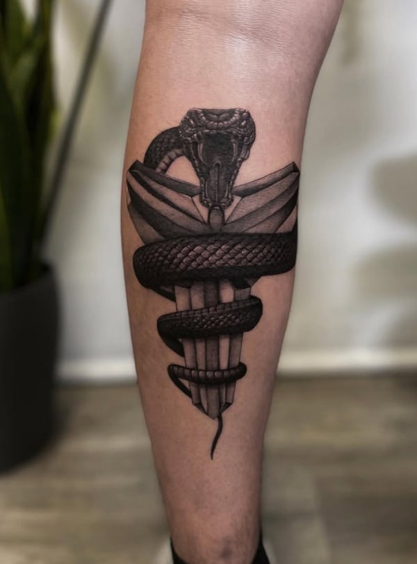 A black and grey tattoo of a snake wrapped around a dagger on the calf, featuring detailed dotwork and bold black lines — by Jian Liang, los angeles