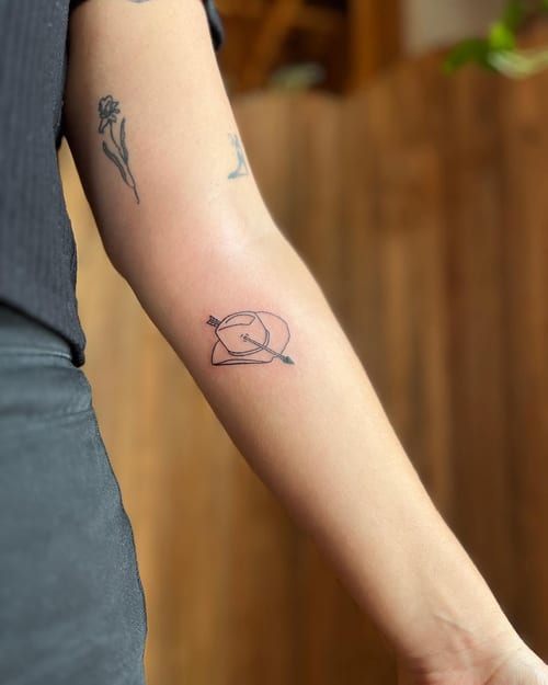 A minimalist black and grey tattoo of a hat with an arrow on the forearm, featuring simple linework — by Dylan Aiello, los angeles
