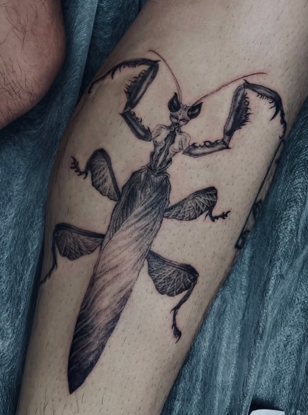 A detailed black and grey realism tattoo of a mantis on the thigh, showcasing intricate linework and shading — by zitronxus, los angeles