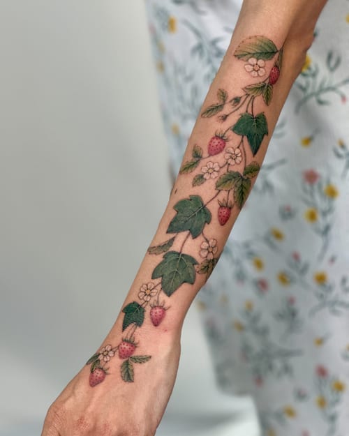 A delicate color tattoo of a strawberry plant with flowers on the forearm, featuring fine line botanical details — by Melanie Benoit, los angeles