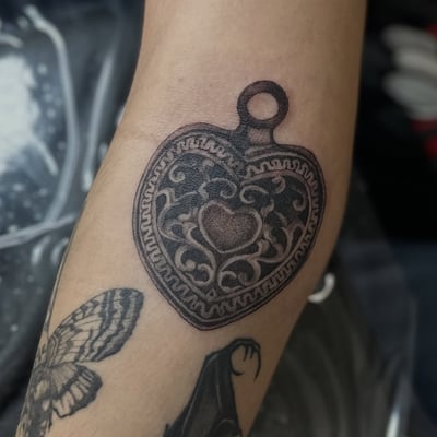 A bold blackwork heart-shaped locket tattoo on the forearm — by Maddie Ramirez, los angeles