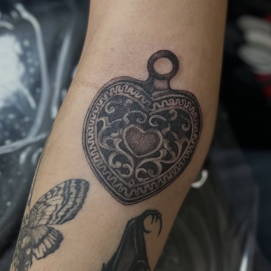 A bold blackwork heart-shaped locket tattoo on the forearm — by Maddie Ramirez, los angeles