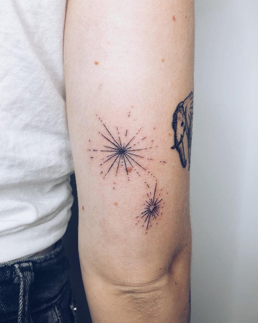 A minimal black linework starburst tattoo on the arm, featuring delicate celestial designs — by Level tattoo, los angeles