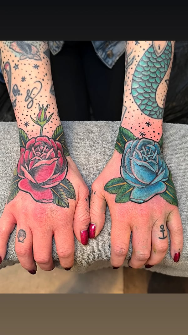 A bold traditional style tattoo of red and blue roses on the hands — by Samuel Connelly, san diego, ca