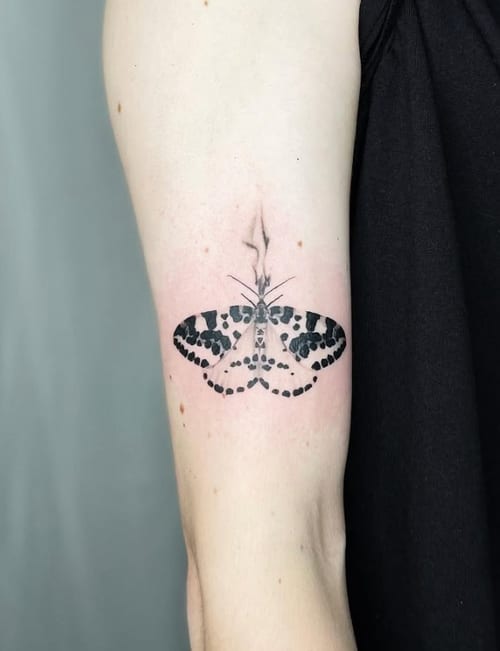 A minimalist blackwork tattoo of a butterfly on the upper arm, featuring simple lines and dot patterns — by Level tattoo, los angeles