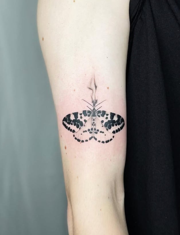 A minimalist blackwork tattoo of a butterfly on the upper arm, featuring simple lines and dot patterns — by Level tattoo, los angeles