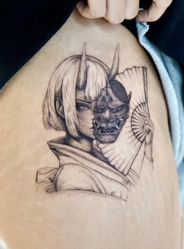 A black and grey tattoo on the thigh depicting a woman with a traditional Japanese mask, featuring detailed linework and shading — by otaybeatdown, orange, ca