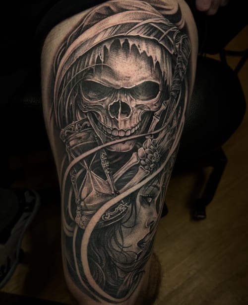 A detailed black and grey realism tattoo on the thigh featuring a skull with a hood and a woman's face intertwined with skeletal elements — by imindisoul, los angeles