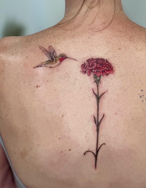 A delicate color tattoo of a hummingbird and carnation flower on the back, featuring fine line and realistic details — by Melanie Benoit, los angeles