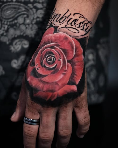 A realistic color rose tattoo on the hand with bold script lettering above it — by Johnny Ayala, los angeles