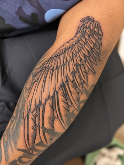 A detailed black and grey angel wing tattoo on the forearm with fine linework and delicate shading — by HEAVY INK, los angeles