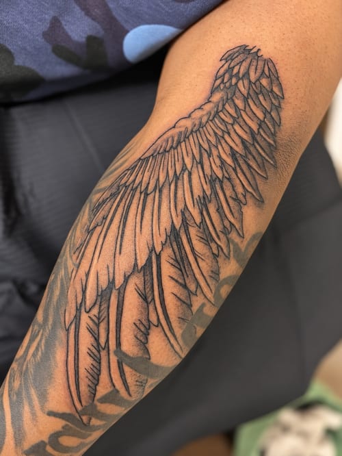 A detailed black and grey angel wing tattoo on the forearm with fine linework and delicate shading — by HEAVY INK, los angeles