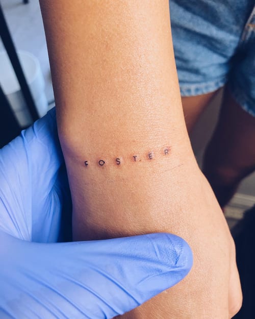 A minimalist black ink script lettering tattoo on the wrist spelling 'FOSTER' — by Level tattoo, los angeles