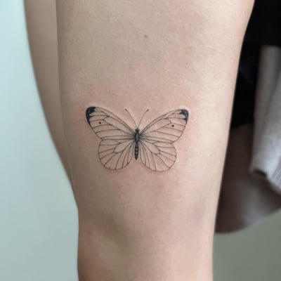 A delicate fine line butterfly tattoo on the thigh, rendered in black and grey with minimalist details — by Melanie Benoit, los angeles