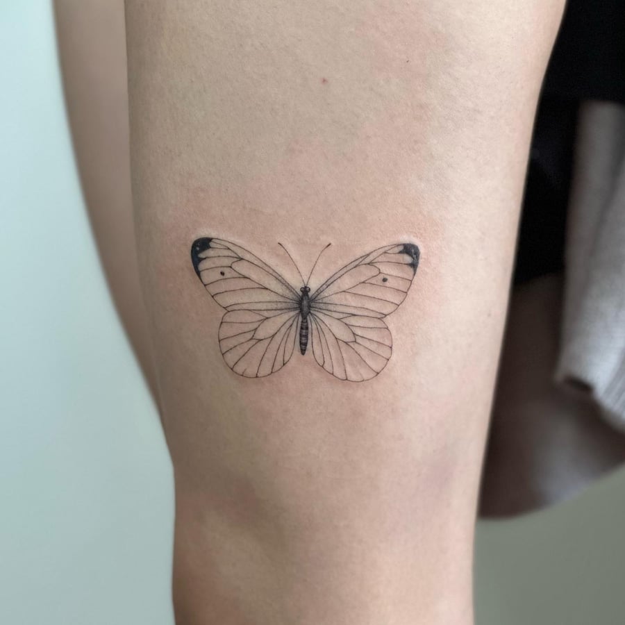 A delicate fine line butterfly tattoo on the thigh, rendered in black and grey with minimalist details — by Melanie Benoit, los angeles