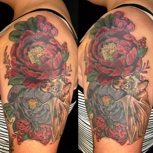 A colorful neo-traditional tattoo of a bat surrounded by flowers on the shoulder, featuring bold lines and ornate details — by Sandra Price, los angeles
