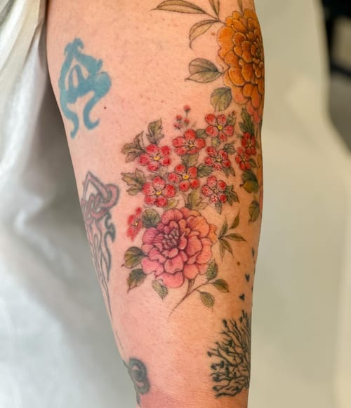 A colorful floral bouquet tattoo on the arm featuring traditional style flowers with delicate and romantic details — by Melanie Benoit, los angeles