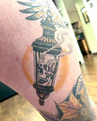 A neo-traditional tattoo of a skull inside a lantern on the leg, featuring a mix of color and black ink with ornate details — by Sandra Price, los angeles