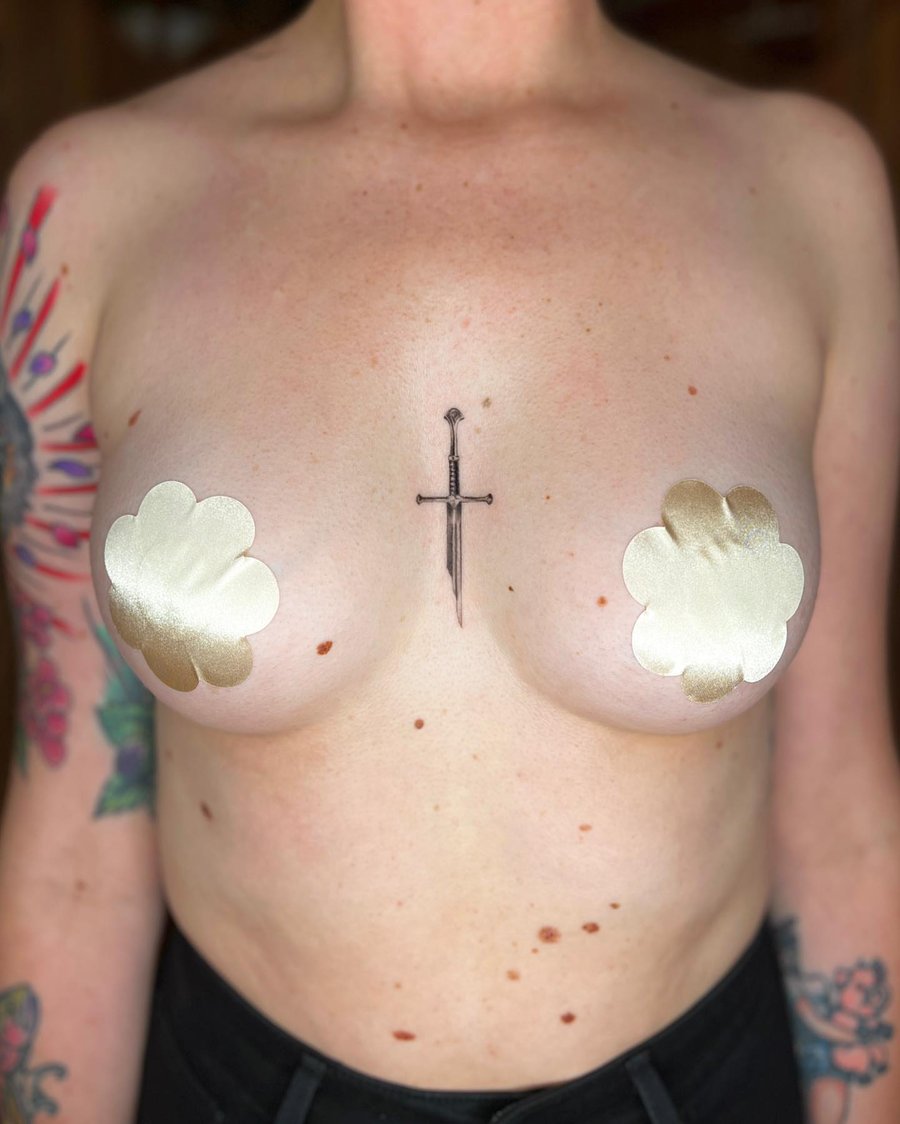 A minimal black and grey fine line sword tattoo on the chest, featuring a simple and clean design — by Dylan Aiello, los angeles
