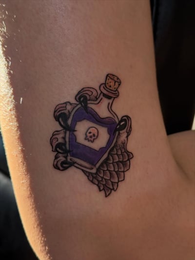 A colorful neo-traditional tattoo of a potion bottle with a skull on the arm, featuring bold outlines and illustrative details — by Kiera Garvin, los angeles