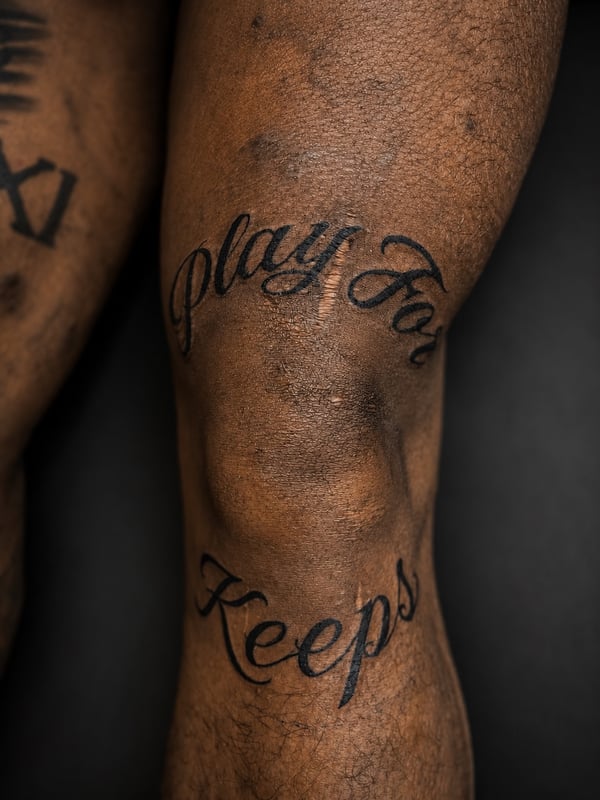 A bold black script lettering tattoo on the leg reading 'Play For Keeps' — by HEAVY INK, chino, ca