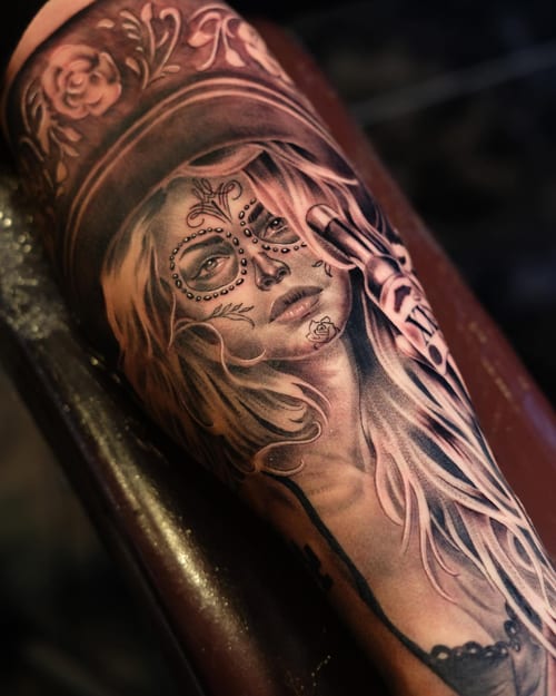 A realistic black and grey portrait of a woman with sugar skull makeup on the forearm, featuring ornate floral details — by Johnny Ayala, los angeles