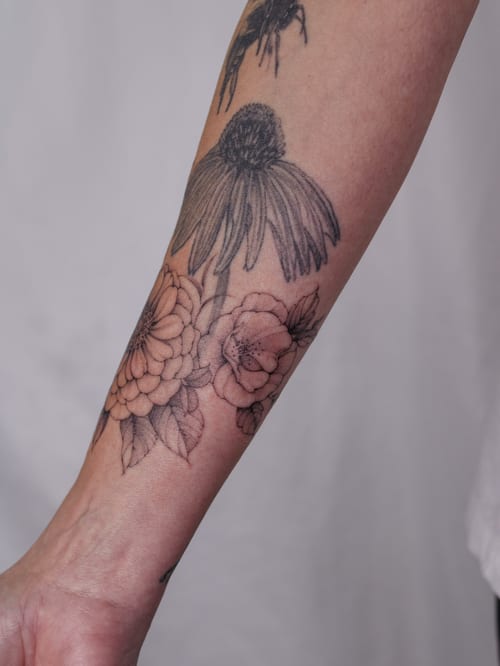 A delicate black and grey floral tattoo on the forearm featuring detailed flower designs — by Melanie Benoit, los angeles