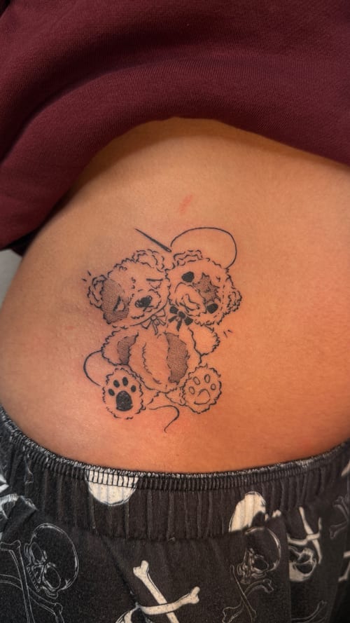 fine line tattoo of two fluffy teddy bears with a bow on the hip — by nj tattooz, los angeles