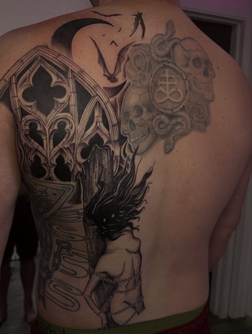 A black and grey back tattoo featuring gothic architecture, a chained woman, and skulls with intricate details — by Maddie Ramirez, los angeles