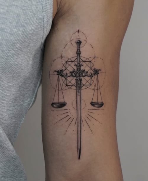 A fine line black and grey tattoo on the upper arm featuring a sword with scales and geometric patterns, symbolizing balance and justice — by Jian Liang, los angeles