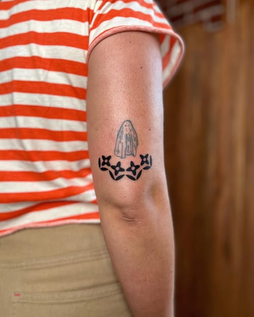 A minimalist black and grey tattoo of praying hands with flowers on the arm — by Dylan Aiello, los angeles