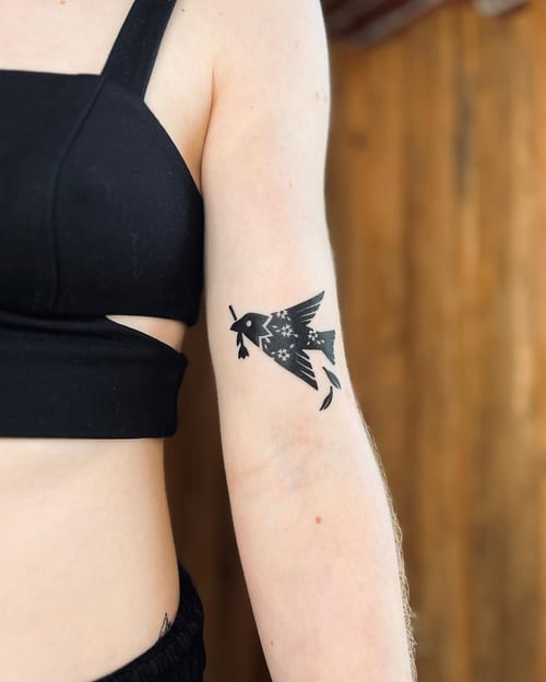 A minimalist blackwork tattoo of a bird with a floral pattern on the upper arm — by Dylan Aiello, los angeles