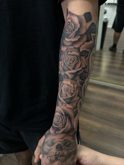 A bold black and grey floral sleeve tattoo with roses and a skull, covering the full sleeve — by Maddie Ramirez, los angeles