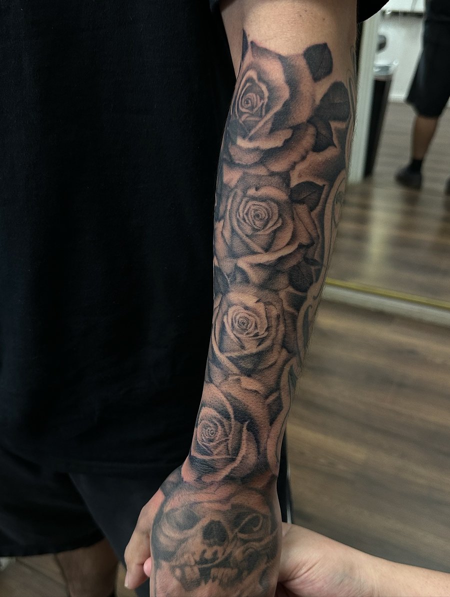 A bold black and grey floral sleeve tattoo with roses and a skull, covering the full sleeve — by Maddie Ramirez, los angeles