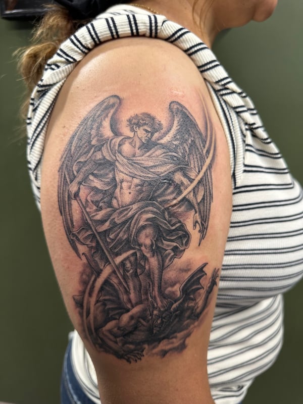 A detailed black and grey realism tattoo of Archangel Michael with a sword, depicted on the upper arm — by Humilde tattoos, los angeles