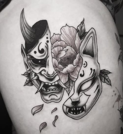 A black and grey tattoo featuring a Japanese demon mask and a fox mask with floral elements on the arm, showcasing bold lines and intricate details — by Shelby Bianco, los angeles