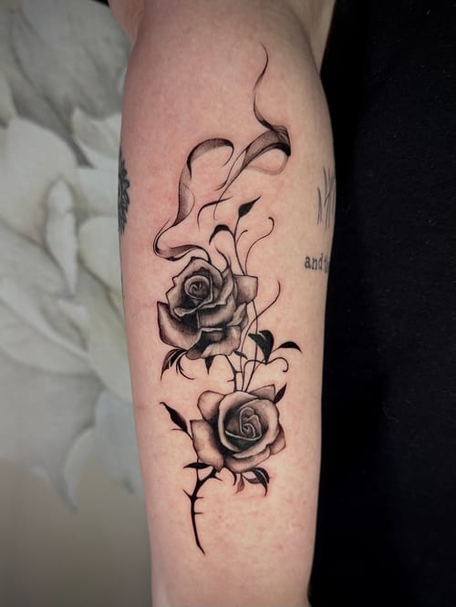 A black and grey tattoo of two roses with fine line details on the forearm, featuring soft shading and delicate linework — by emily, los angeles