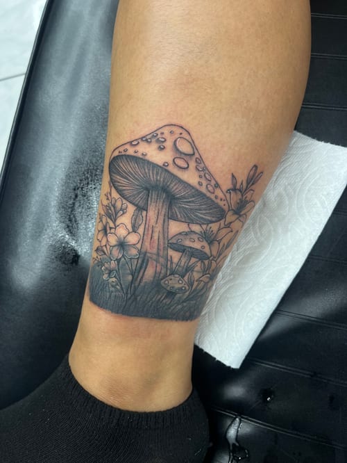 A black and grey tattoo of mushrooms surrounded by flowers on the calf, featuring detailed linework and shading — by Mr._Folks, los angeles