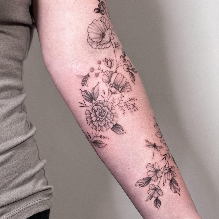 A delicate black and grey floral arrangement with a bee and dragonfly on the forearm, featuring fine line work and botanical elements — by Melanie Benoit, los angeles