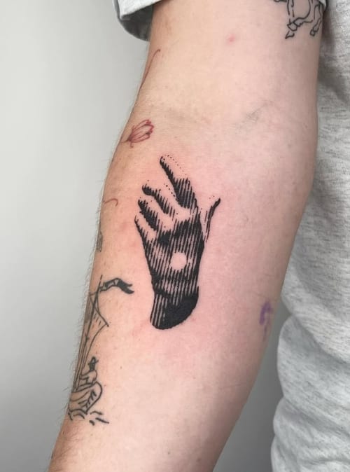 A black and grey tattoo of a hand with a circular cutout, featuring bold lines and a minimalist design on the forearm — by Level tattoo, los angeles